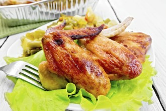 Fried chicken wings with vegetables and salad leaves on a plate, fork on the background light