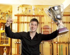 Happy proud winner man with big trophy silver cup in billiard club