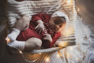 A cute newborn baby in xmas clothes sleeping in a basket on the floor against a Christmas