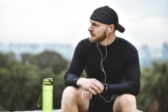 Muscular bearded athlete checking burned calories on smart watch after good workout session on city
