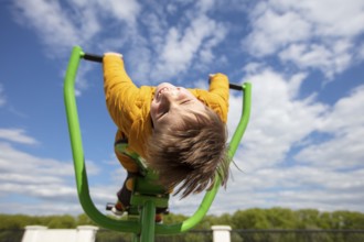 Funny little boy on a swing with his head down. Happy child on a walk. Ten year old boy against the