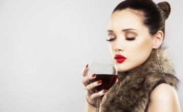 Beautiful woman with dark makeup and red lipstick posing on light grey background. Drinking glass