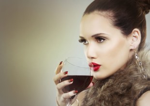 Beautiful woman with dark makeup and red lipstick posing on light grey background. Drinking glass