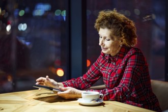 Mature woman with blond curly hair checks mail and social media notifications via tablet, smiling