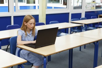 Primary school caucasian girl using a laptop in an empty classroom