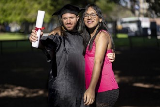Young recently graduated man, dressed in cap and gown, with his degree in hand, celebrating with