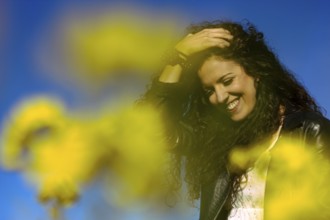 Close up portrait of a young woman holding her hand on her head and smiling in a field of yellow