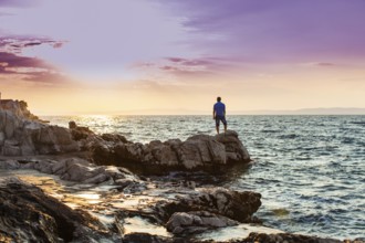 Yung man standing on a rock and looking at the sunset on the sea