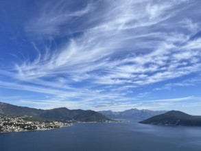 White cirrus clouds in the blue sky over a mountain range near the sea.