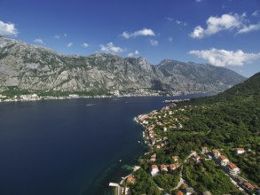 Resort town on the shores of the Bay of Kotor among green trees at the foot of the mountains.