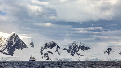 A ship in front of a snow-covered mountain range in a cold, cloudy Antarctic scenery, cruise ship
