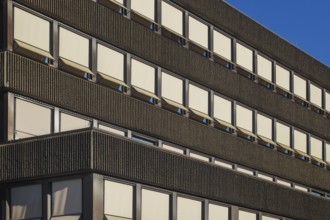 Sunlight illuminating rows of windows and awnings on a modern building facade, creating a