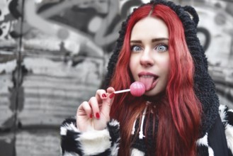 Portrait of a young beauty teen girl in a hoodie with a delicious pink lollipop, posing against a