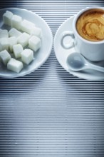 Cup of cappuccino coffee saucer teaspoon sugar cubes on striped background