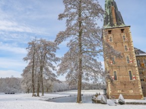 Castle on the water surrounded by snow-covered trees and wintry landscape under a blue sky,