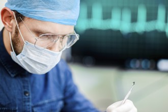 A surgeon in protective gear handling a medical instrument with an ECG in the background