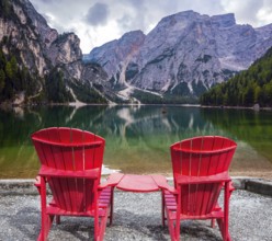 Two comfortable red deck chairs on the shore of the lake. Water reflects the surrounding mountains