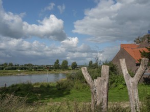 A peaceful riverside with expansive nature under a partly cloudy sky and a rustic ambience,