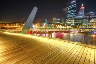 Wooden walkway of Elizabeth Quay pedestrian bridge illuminated by night at Elizabeth Quay marina, a