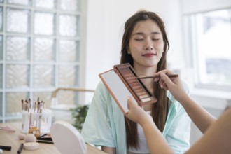 Makeup artist. Professional makeup artist working with beautiful young asian woman applying
