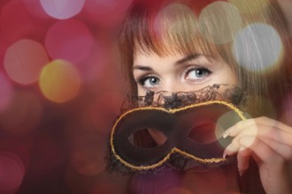 Beautiful young woman in carnival mask over blurred background