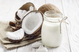 Mason jar of milk or yogurt on hemp napkin on white wooden table with coconut aside