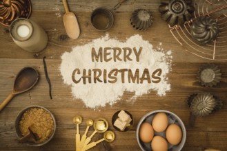 Collection of ingredients and utensils for baking on a dark wooden table with the words Merry