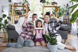 Traditional family with child are enjoying new home, sitting on the sofa and holding the roof.