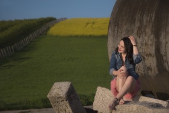 Attractive girl, casual dressed, with bare feet, eyes closed and smiling, sitting on a rock, in