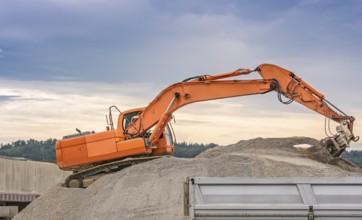 Orange excavator, climbed on a ballast pile, loading material in a trailer