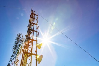 A low angle view of two mobile communication data transmitter and GPS signal towers, against a blue