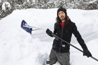 Satisfied and happy man smiling as he standing between snow piles holding a shovel to removing