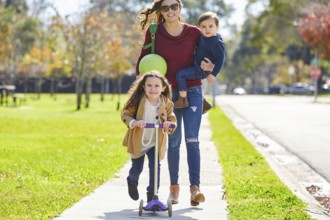 Mother daughter and son family in the park walking with ball and skate scooter