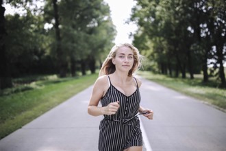 Woman jogging on a tree-lined road wearing a striped outfit