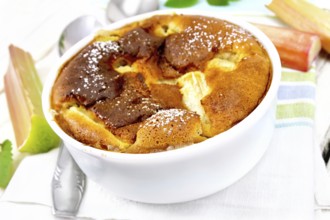 Pie klafouti with rhubarb in the bowl, mint and rhubarb stalks on a napkin against light wooden
