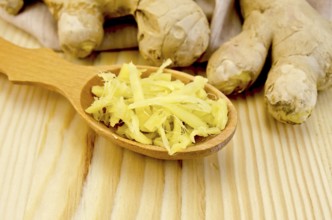Wooden spoon with grated ginger, ginger root on a napkin on the background of wooden board