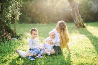 Mother is sitting on the lawn with her two children.