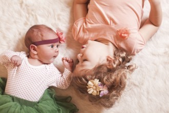 Little girl with her newborn sister on a fur carpet