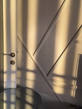 An interior space bathed in sunlight, casting geometric shadows across a wall and door