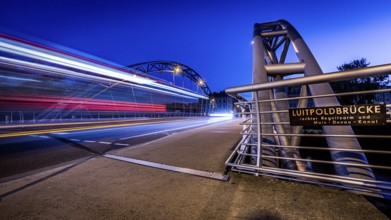 Night scene of an illuminated bridge with passing cars and an information sign, Luitpoldbrücke