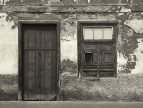 Monochrome image of the front of an old abandoned house with shuttered windows and locked wooden
