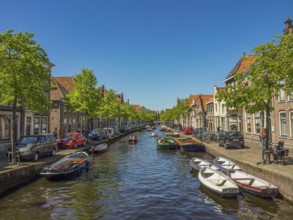 A long canal lined with boats, cars and historic buildings on a sunny day, alkmaar, the netherlands