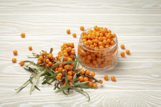Sea buckthorn ripe berries in glass jar and branches with leaves top view on white wooden rustic