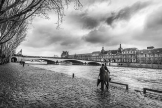 Black and white image with the Seine River, its shore where people walk, an old bridge and the