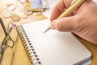Close-up image with a blank math notebook and a man's hand holding a pen. In the background there