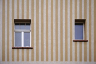 A house wall with a yellow and beige striped wall painting with two windows