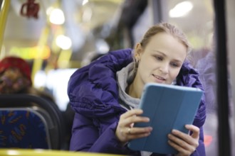Young woman in purple jacket using her touchpad during the ride in the bus