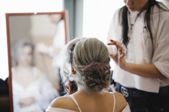 Stylist makes the bride in front of the mirror a beautiful hairstyle.