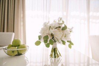 Bridal bouquet of white peonies, sweet pea and branches of eucalypt tree on a glossy white table