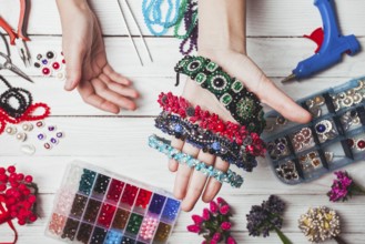 Plastic berries, flowers, beads and instruments for doing handmade headbands. Top view with hands